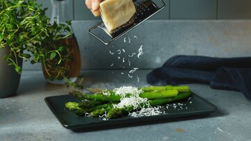 Cheese being grated over a tray of asparagus.